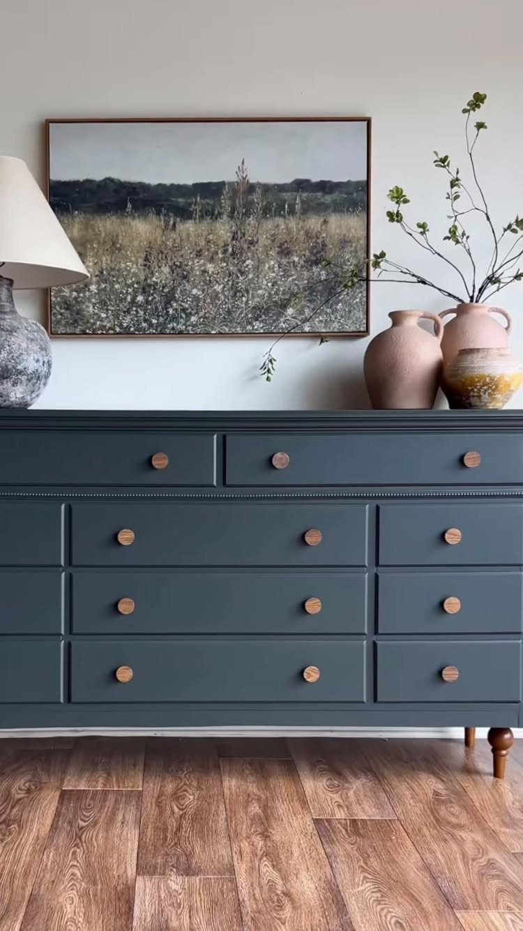 Dark teal painted dresser with wooden knobs and a landscape painting above it.
