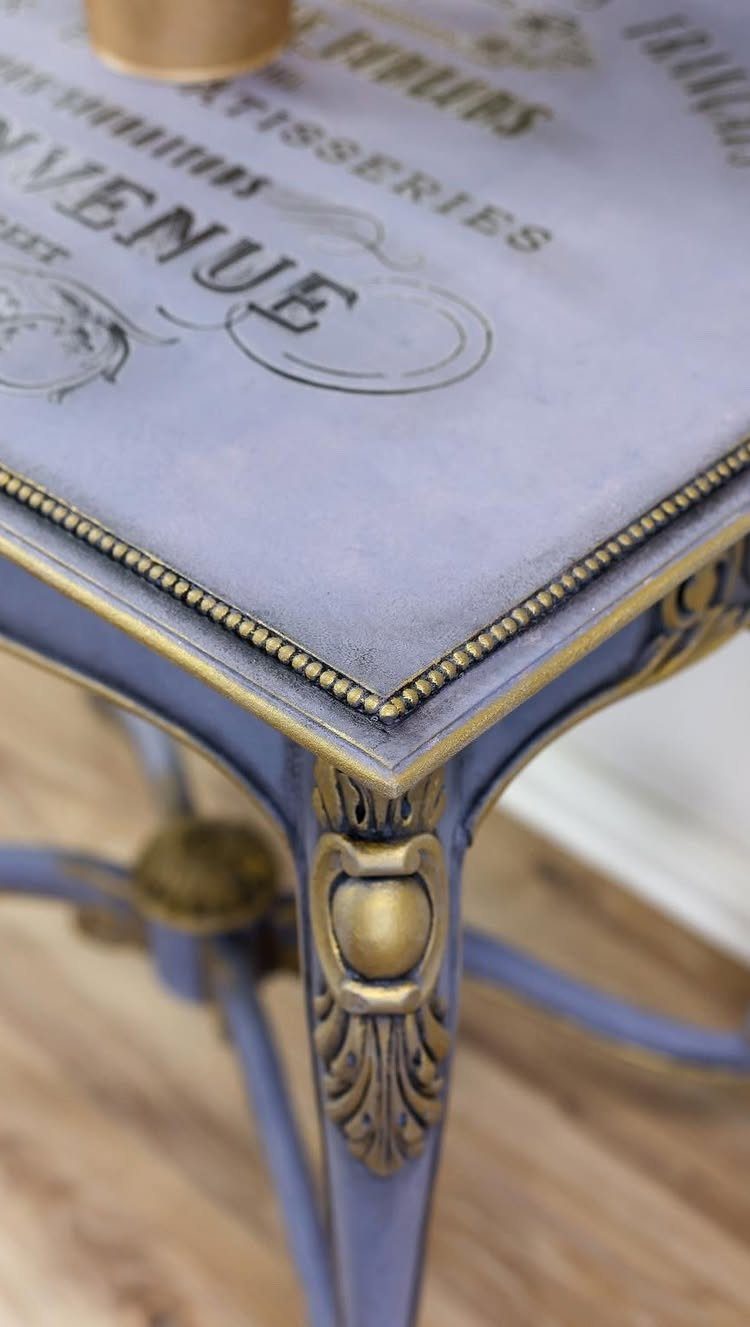 Purple painted side table with gold ornate details and vintage typography on top.