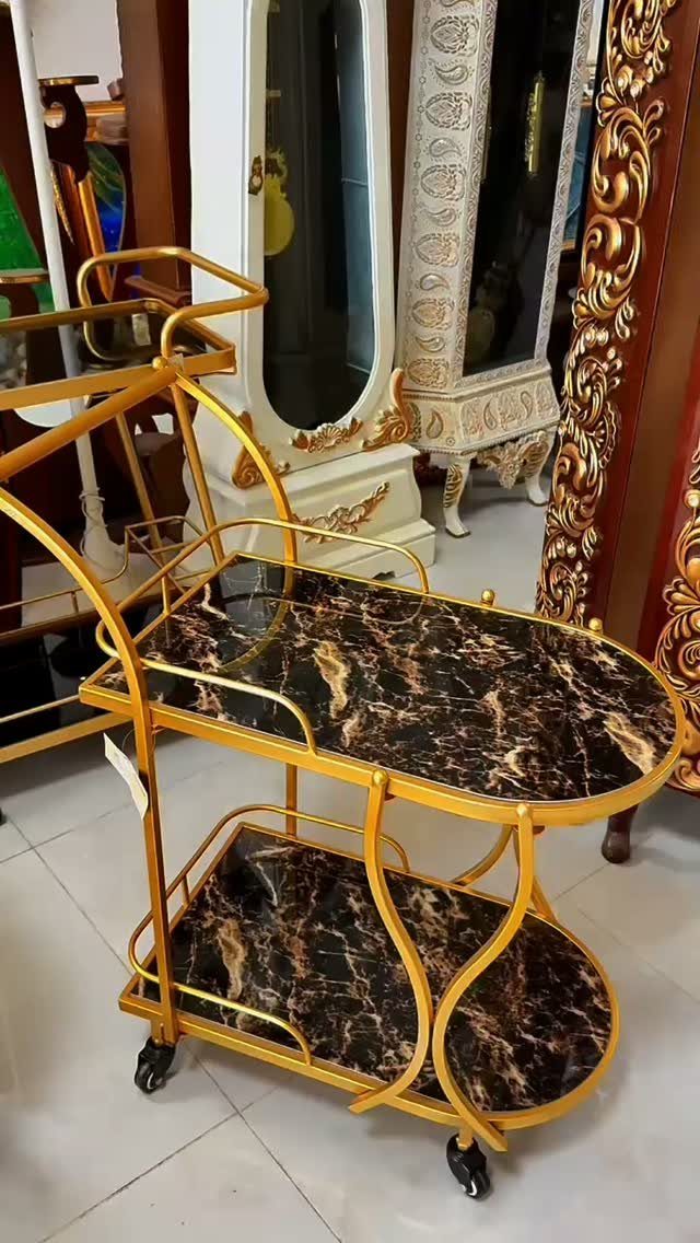 Gold metal drinks trolley with dark brown marble patterned shelves in a showroom
