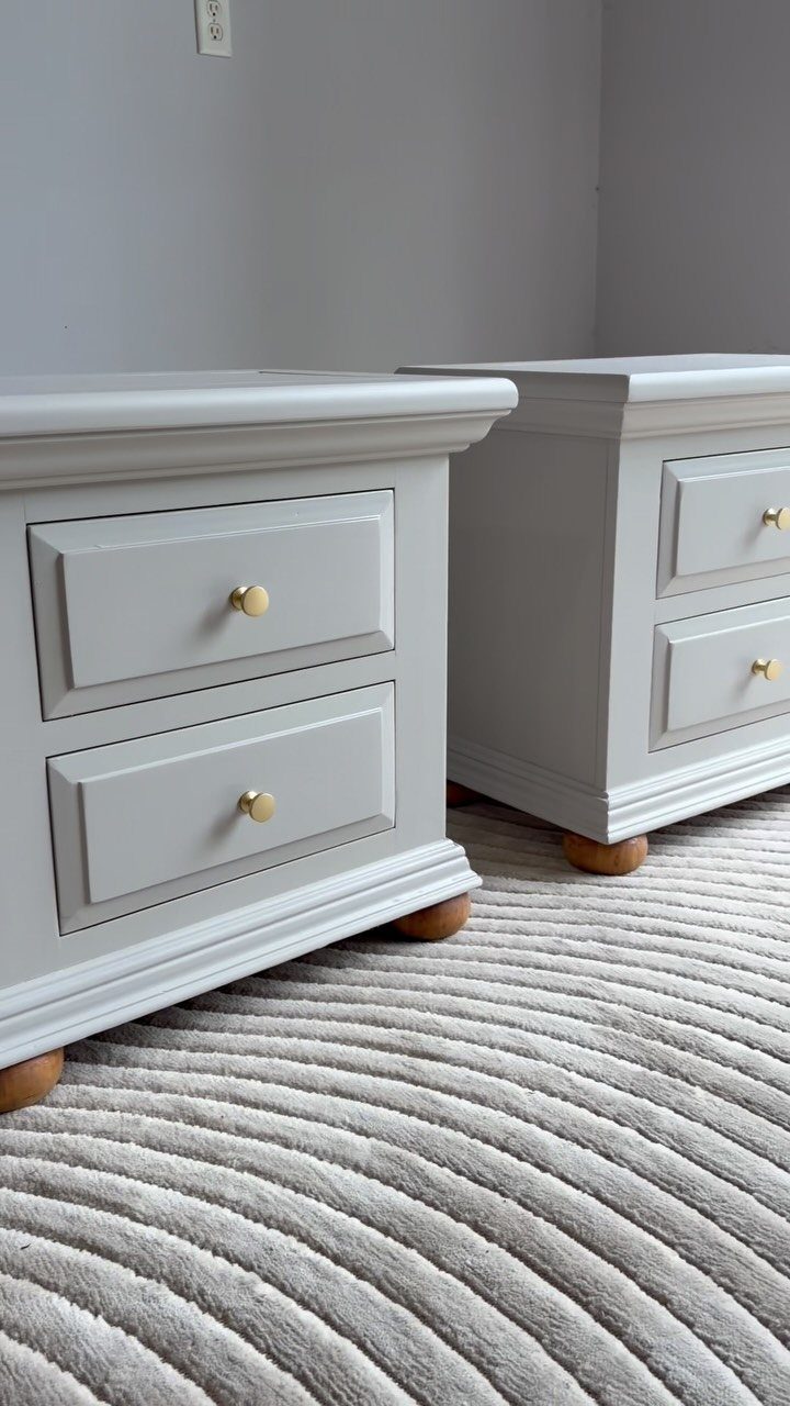 Two light grey painted nightstands with gold knobs on a striped rug.