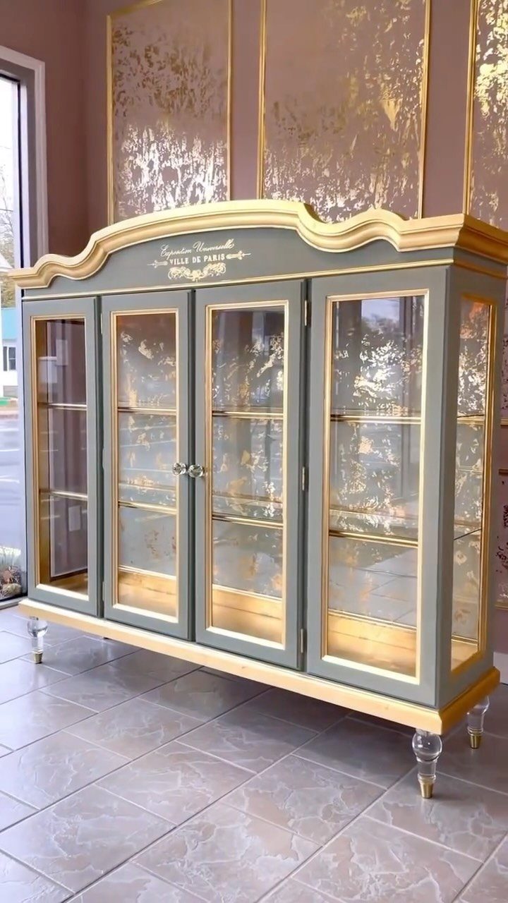 Sage green and gold ornate display cabinet with glass doors on tiled floor