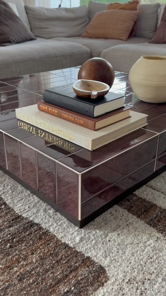 Glossy purple tiled coffee table with books and decor on a textured rug.