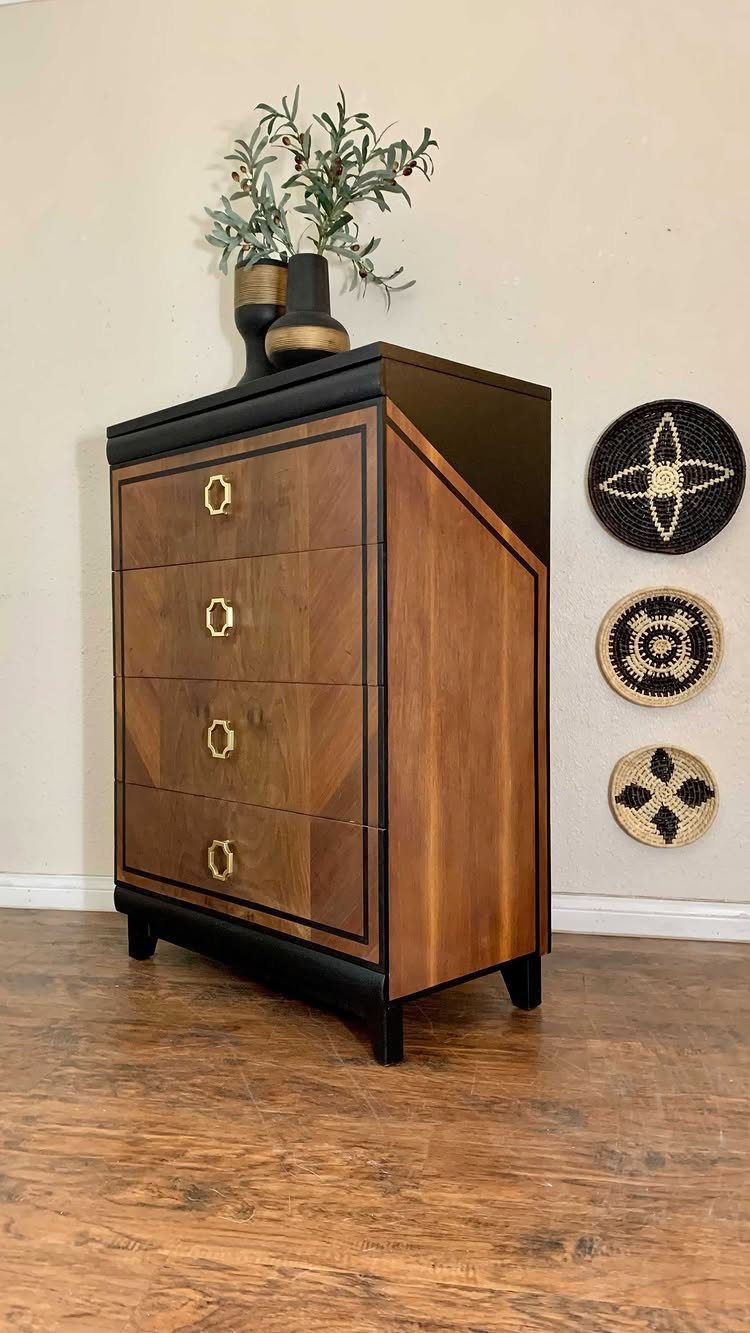 Wooden dresser with black trim and gold knobs against a plain wall.