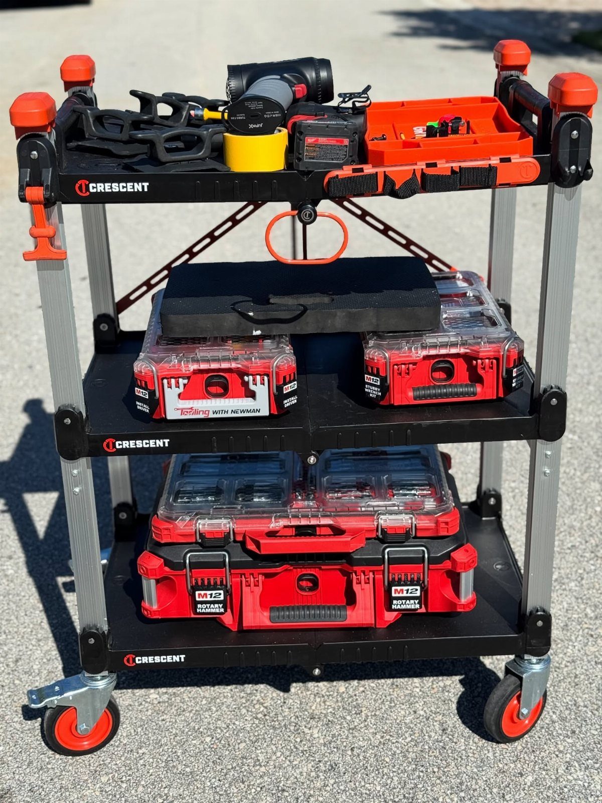 Three-tier rolling tool cart loaded with red toolboxes and power tools on pavement.