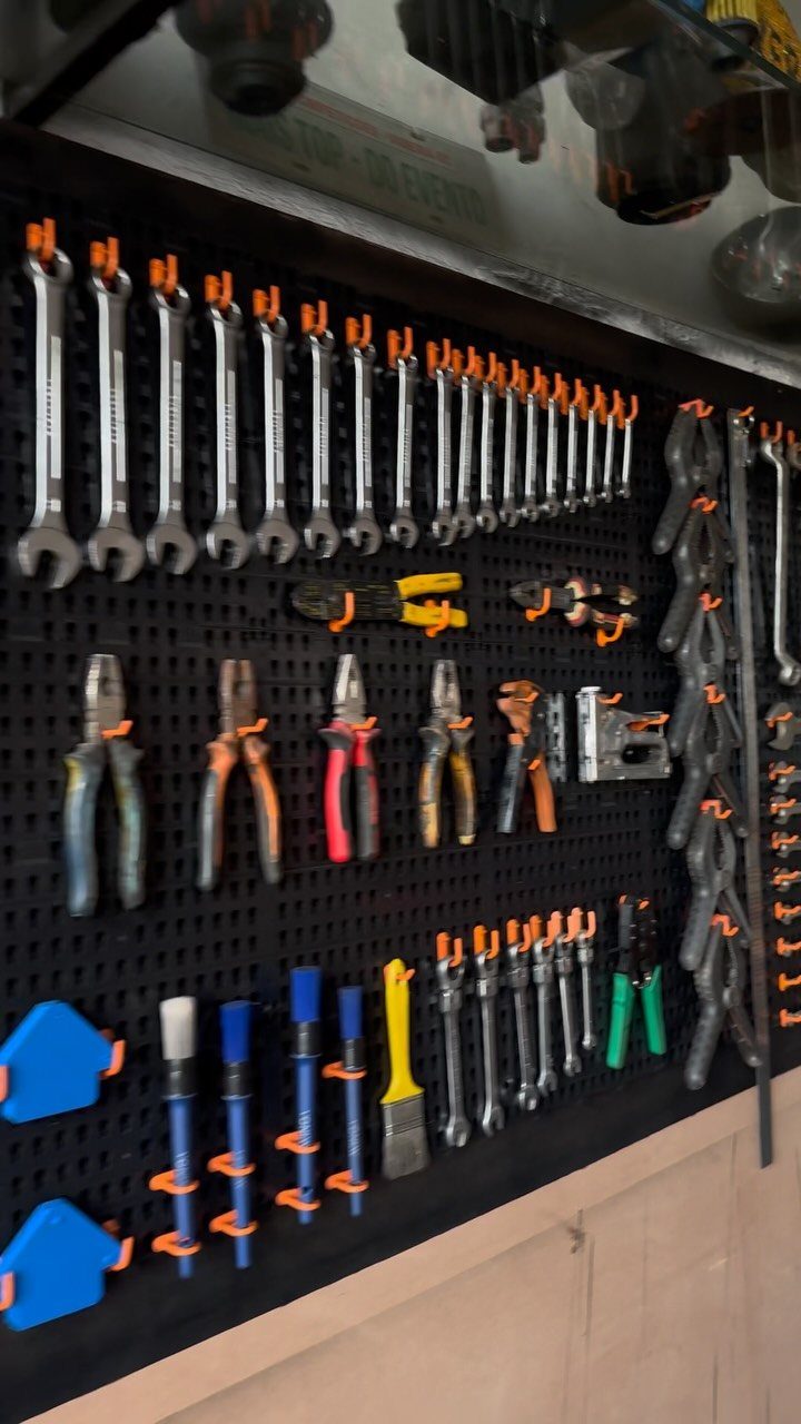 Black wall-mounted pegboard with organized hand tools and orange hooks in a workshop.