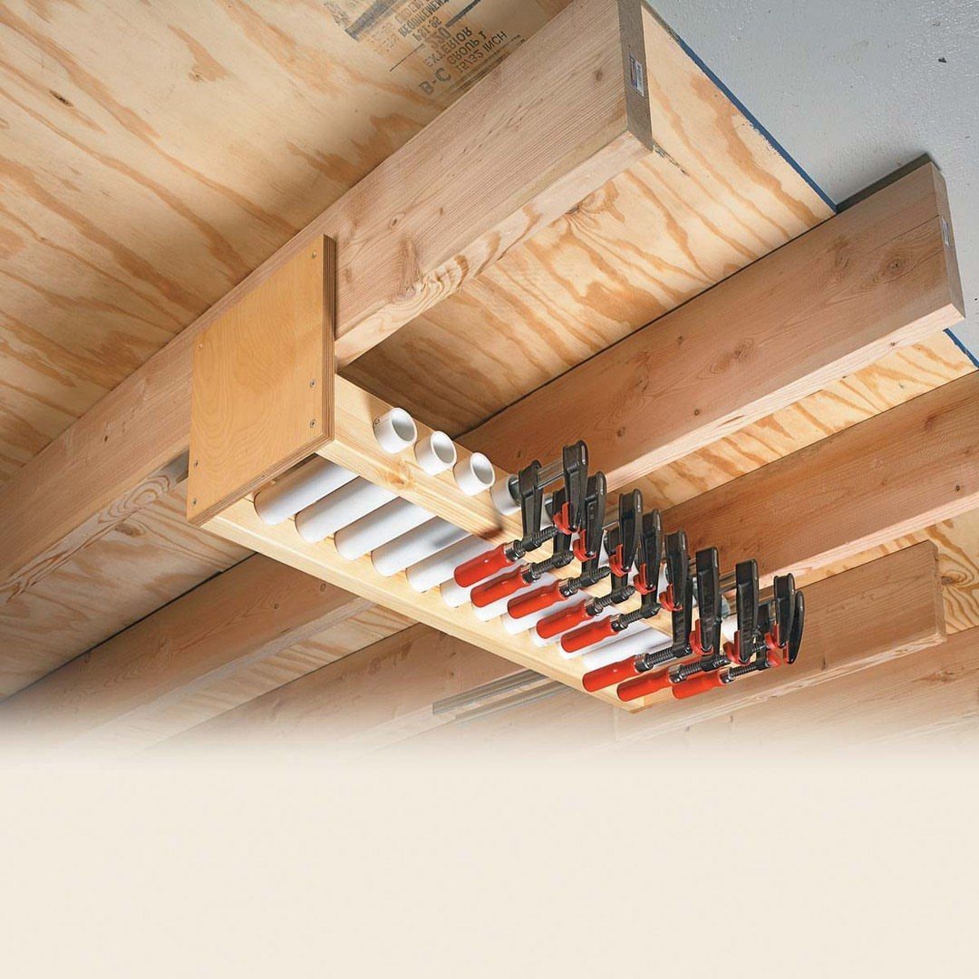 18 Garage Woodshop Ideas for Storage, Power, and Layout 4 Wooden ceiling rack holding red bar clamps and white PVC pipes in a garage.