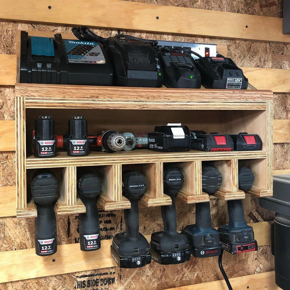 18 Garage Woodshop Ideas for Storage, Power, and Layout 15 Wooden tool rack holding cordless drills and batteries on a plywood garage wall