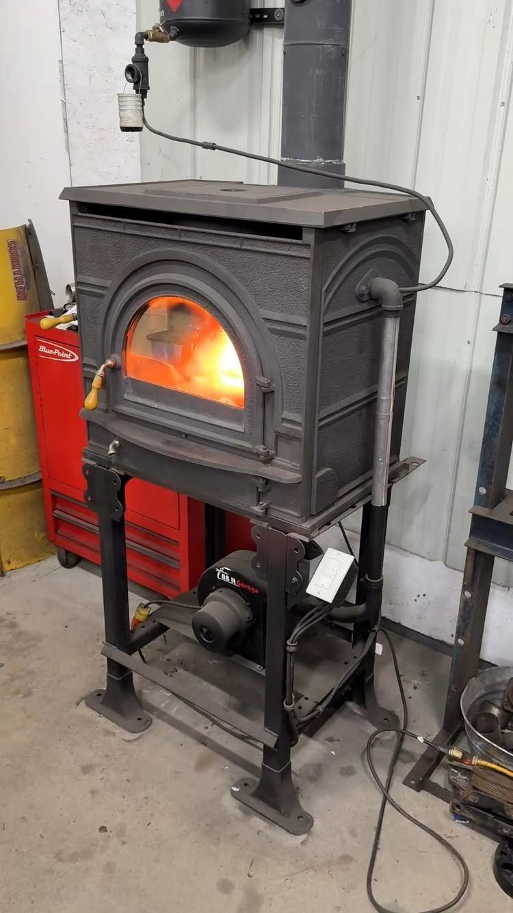 18 Garage Woodshop Ideas for Storage, Power, and Layout 18 Cast-iron wood-burning stove with glowing fire on a metal stand in a garage.