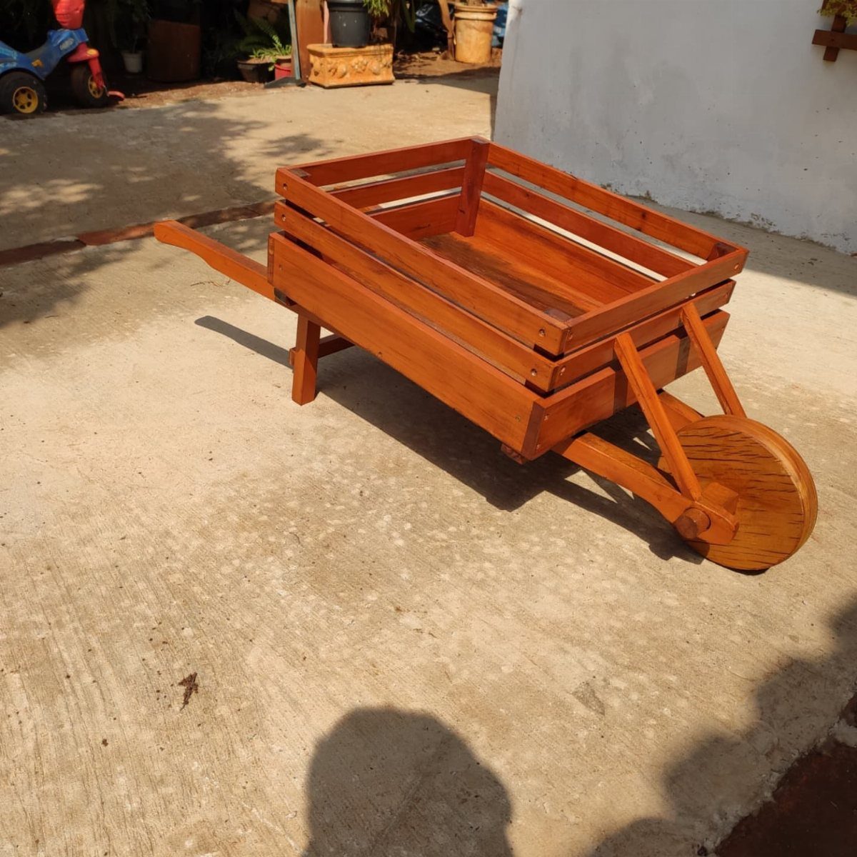 Wooden garden cart with a single large wheel on a concrete patio.