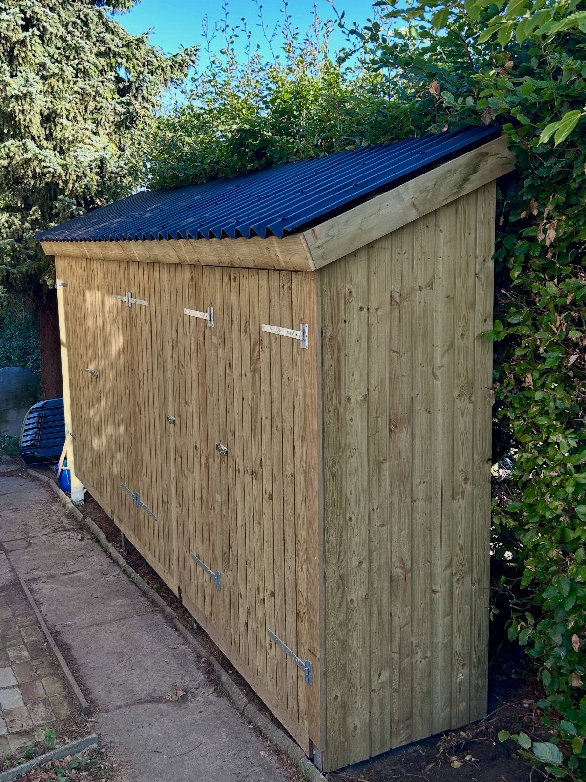 Wooden garden shed with a black corrugated roof standing on a concrete path.