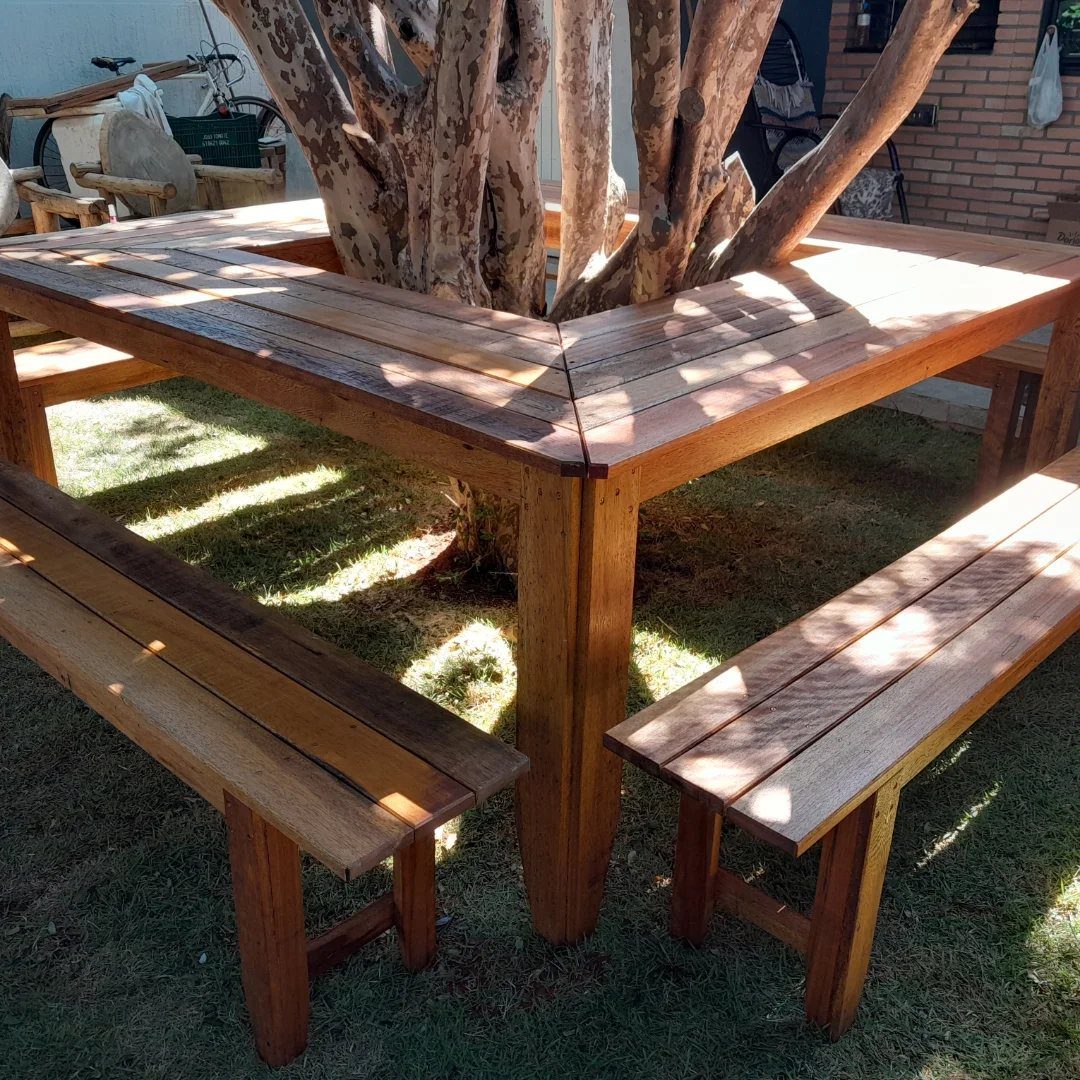 Square wooden outdoor dining table and benches built around a large tree trunk.