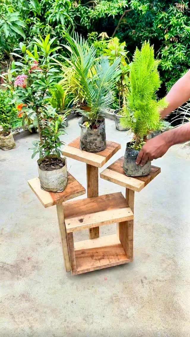 Multi-tiered wooden plant stand holding three potted green plants in a garden setting.