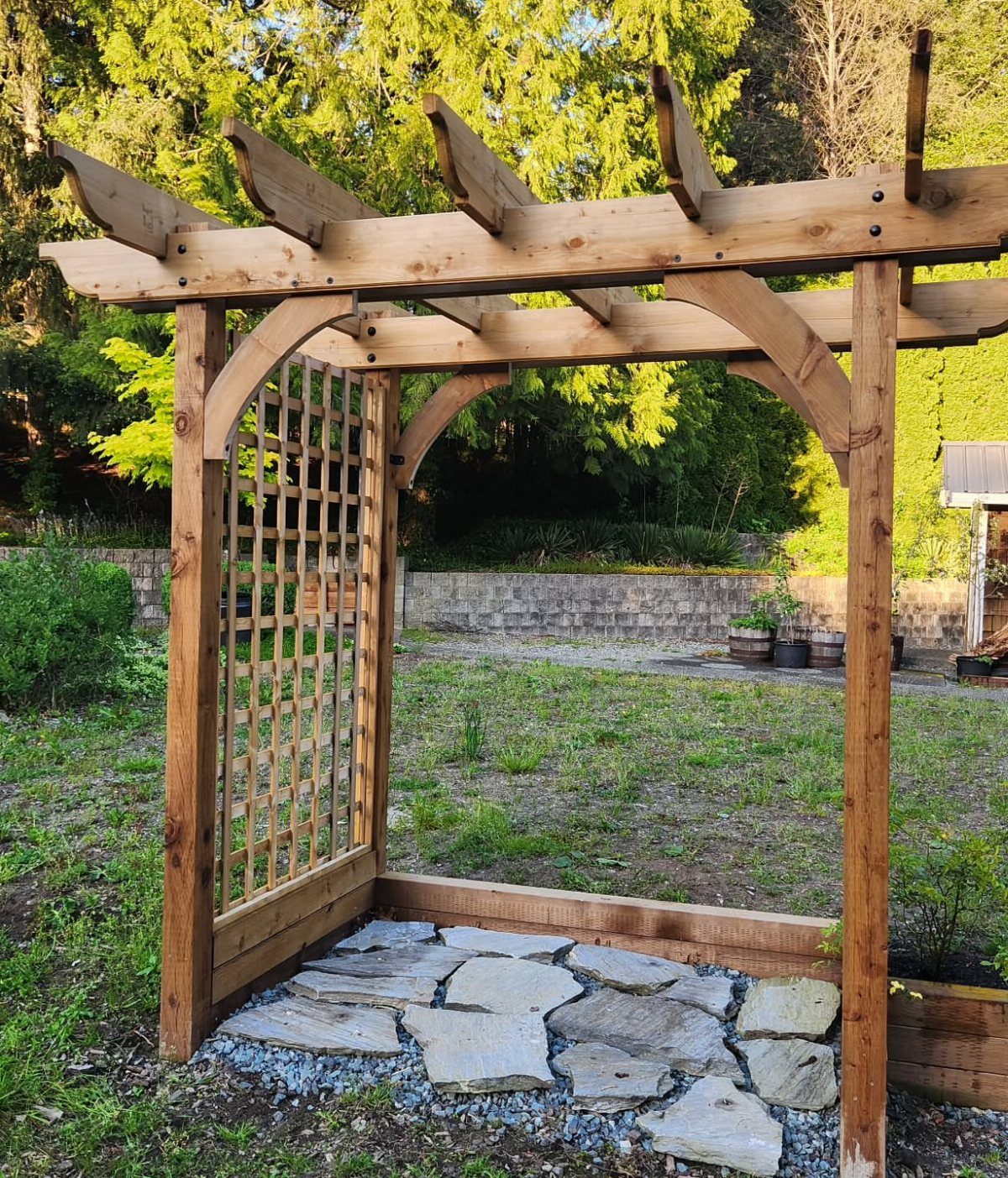 Wooden garden pergola with a lattice trellis wall over a stone patio.