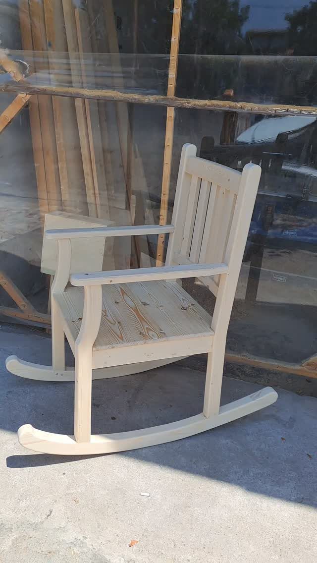Unfinished wooden rocking chair with slatted back and curved rockers on concrete.