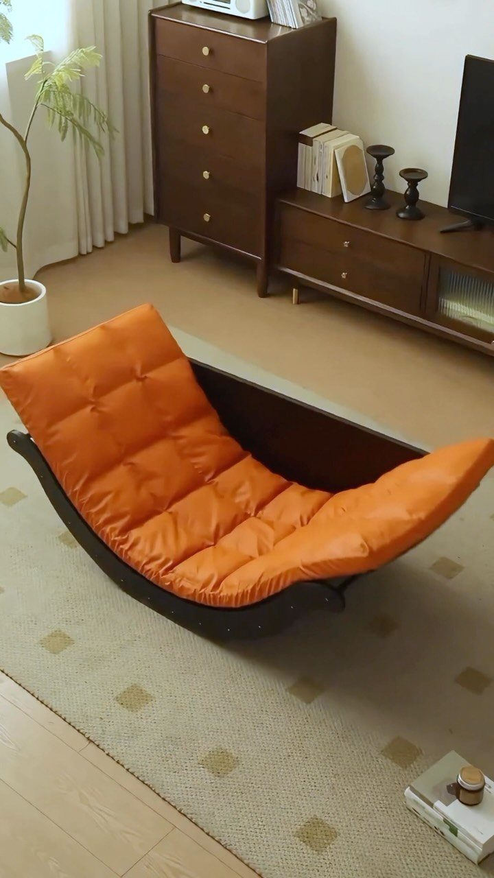 Curved wooden rocking chair with a tufted orange cushion in a minimalist living room.