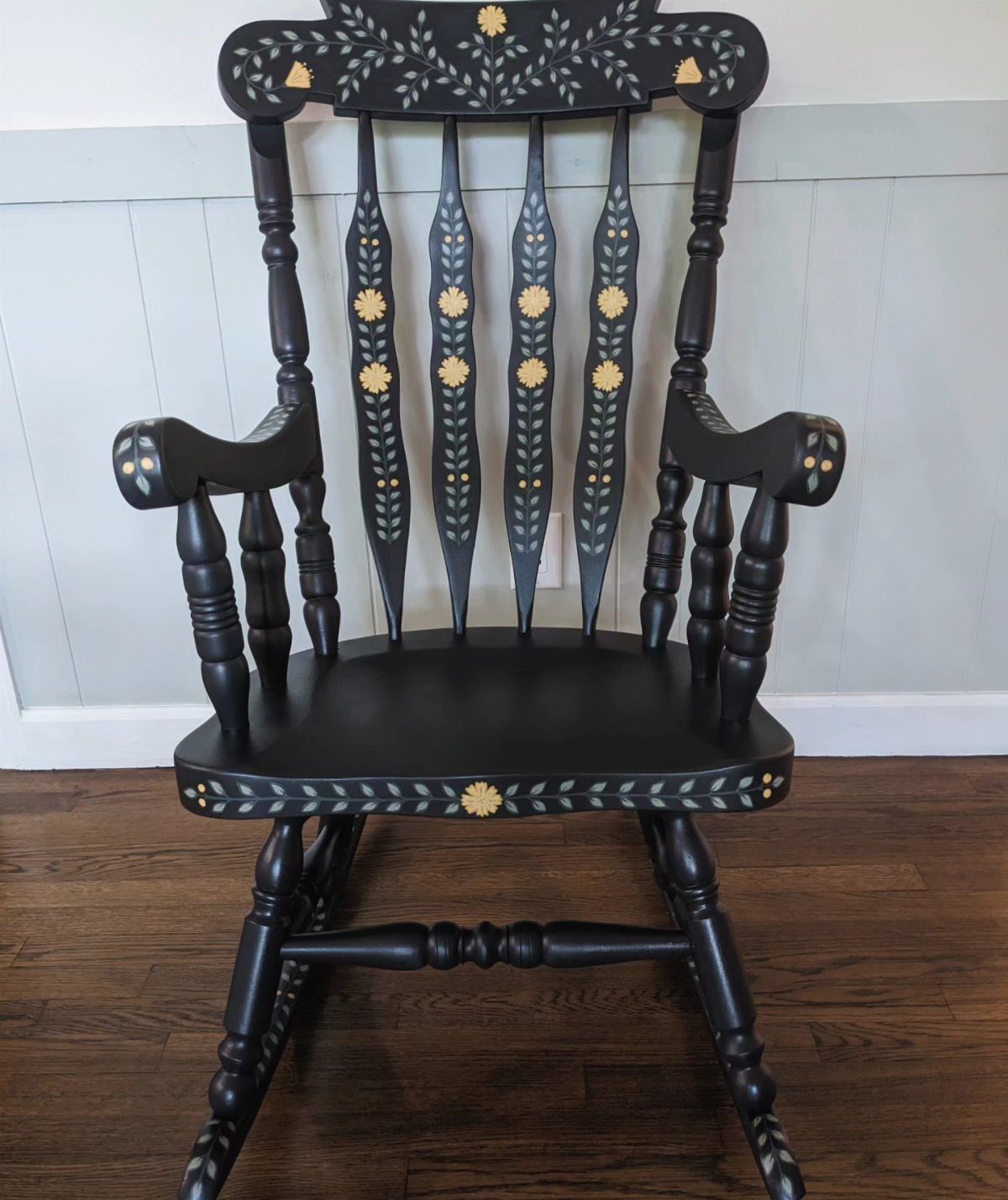 Black wooden rocking chair with yellow and white floral painted decorations.