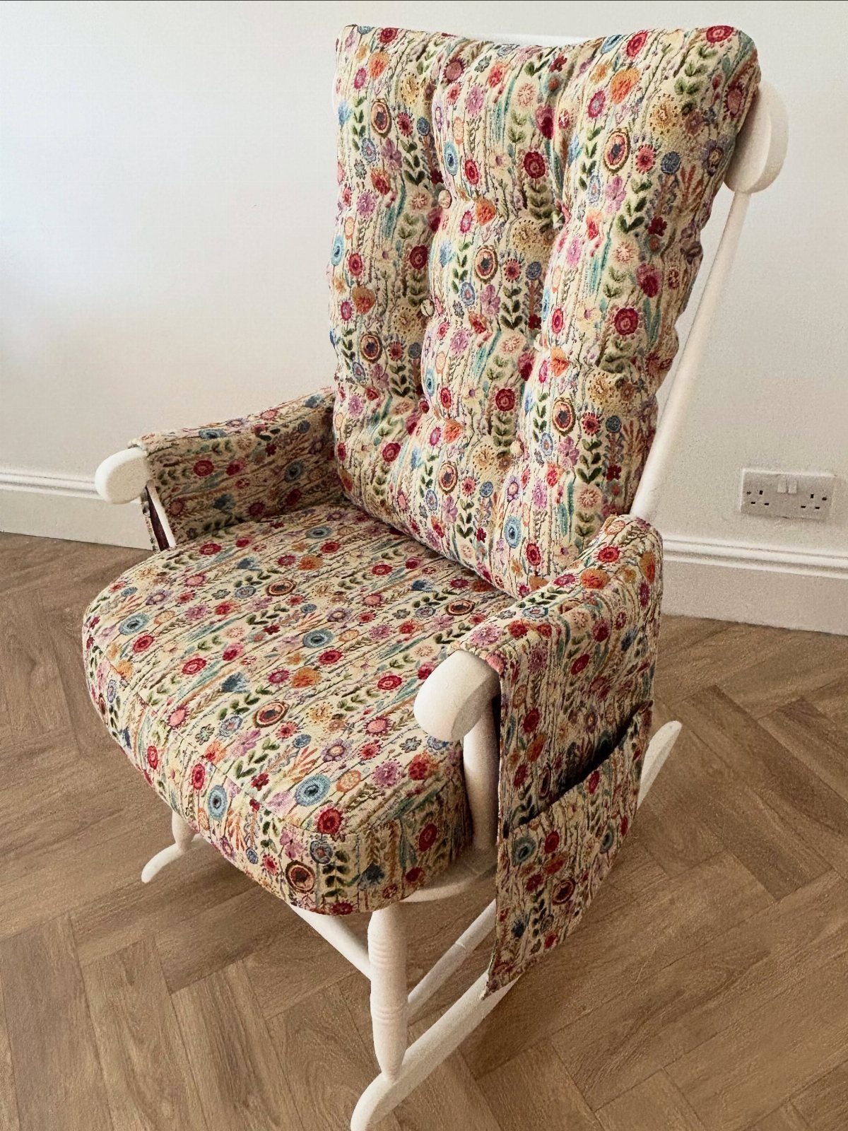 Floral upholstered white wooden rocking chair on a herringbone wood floor.