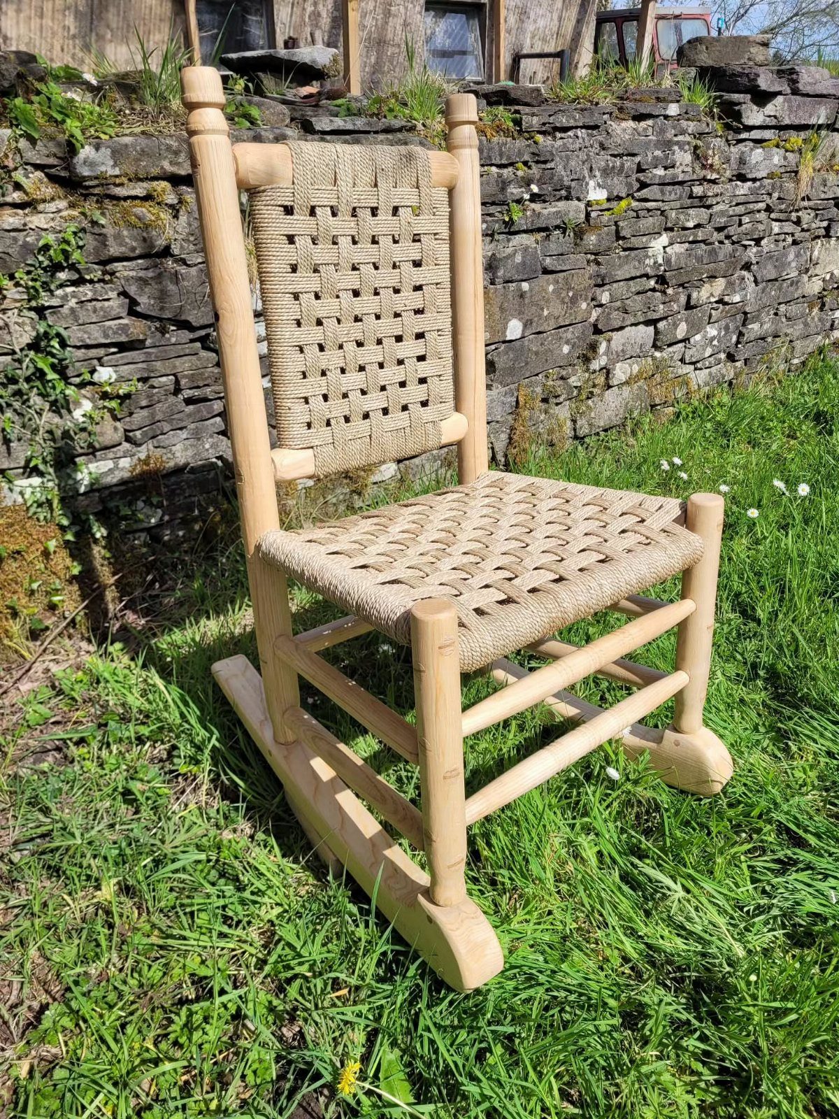 Wooden rocking chair with woven rope seat and backrest on a grassy lawn.