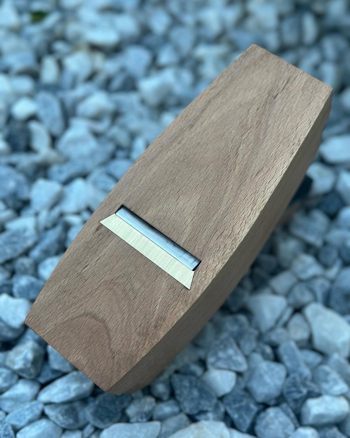 7 Homemade Tools for Woodworking You Can Build 4 Handmade wooden block plane with metal blade resting on grey pebbles.