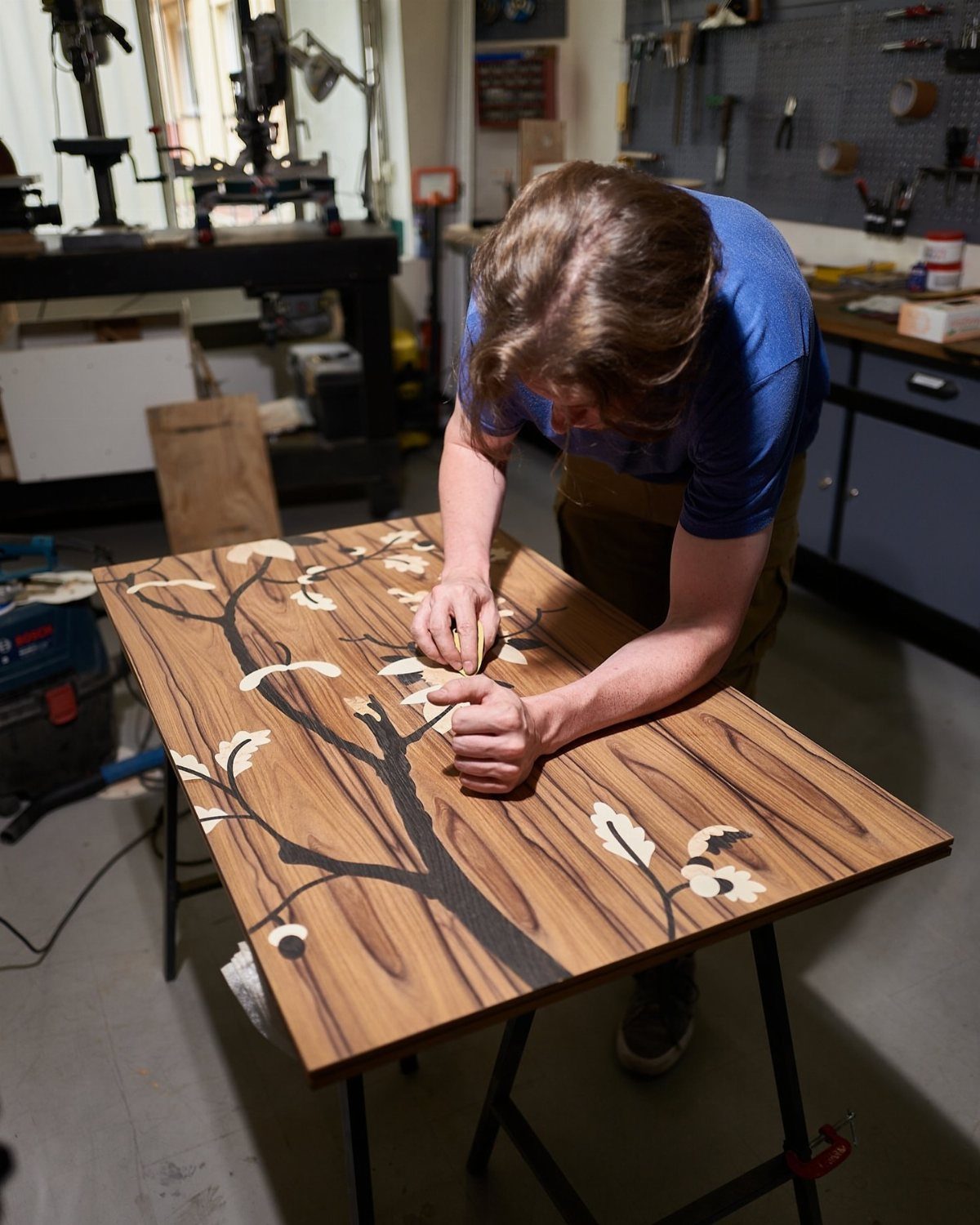 Inlays in Wood: 9 Ideas for Veneer, Resin and Metal 7 Person working on a wooden tabletop with a light wood tree inlay design.