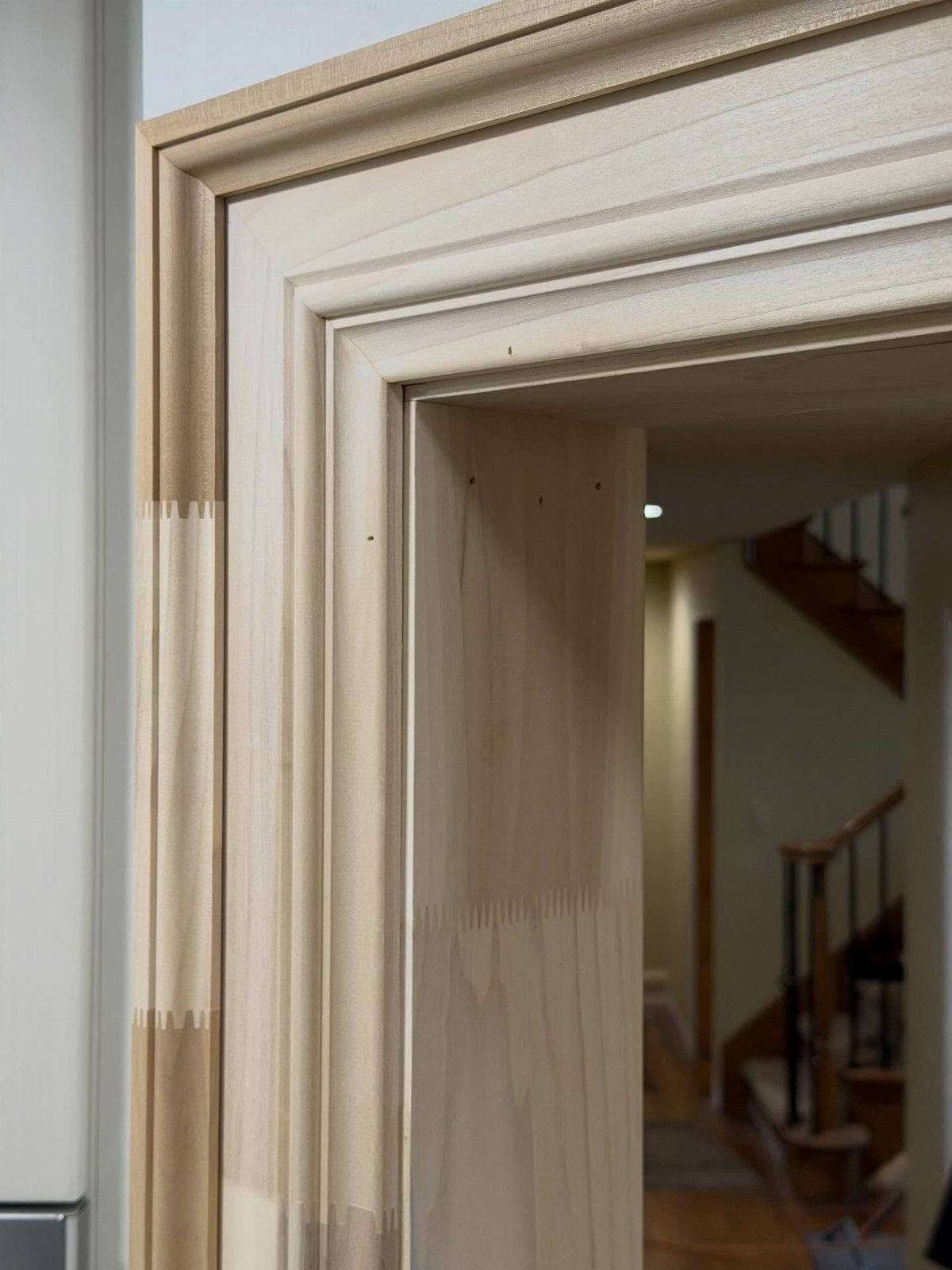 Mitered joints on a light-colored wooden door frame with decorative molding.