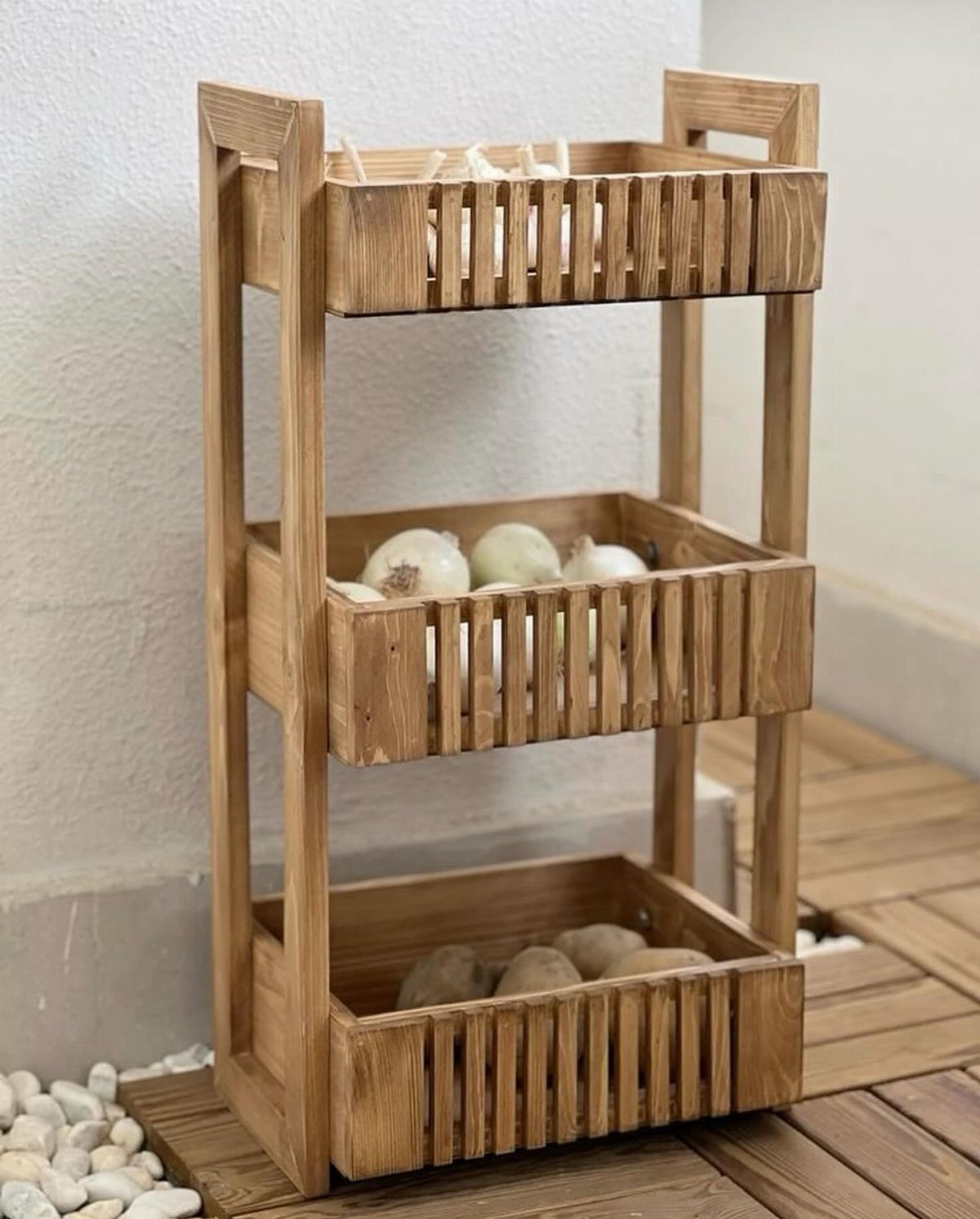 18 Kitchen Woodworking Projects for Storage and Gifts 12 Three-tiered wooden produce stand holding onions and potatoes on a wooden deck.