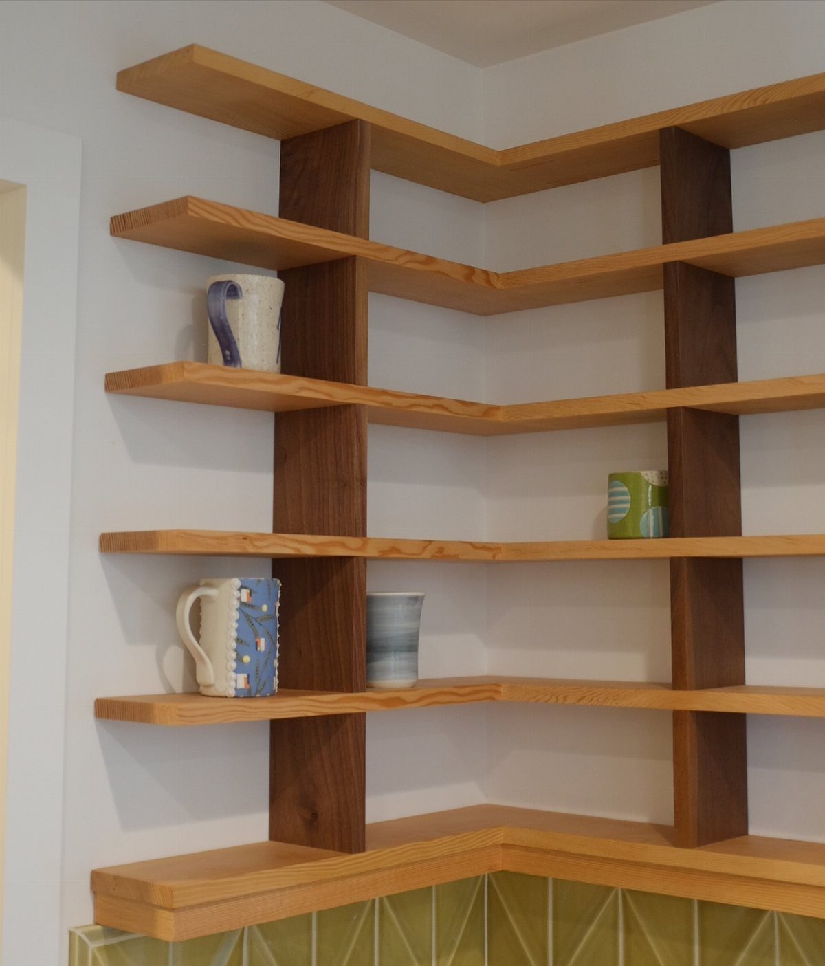 18 Kitchen Woodworking Projects for Storage and Gifts 5 Wooden floating shelves in a kitchen corner holding ceramic mugs and pitchers.