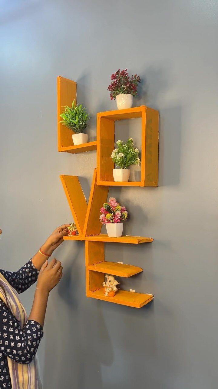 Orange wooden wall shelf shaped like the word LOVE with small potted plants.