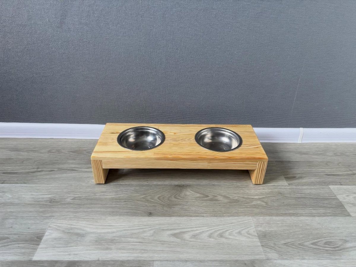 32 Mini Wood Projects for Beginners and Scrap Wood 15 Wooden elevated dog bowl stand with two stainless steel bowls on grey flooring.