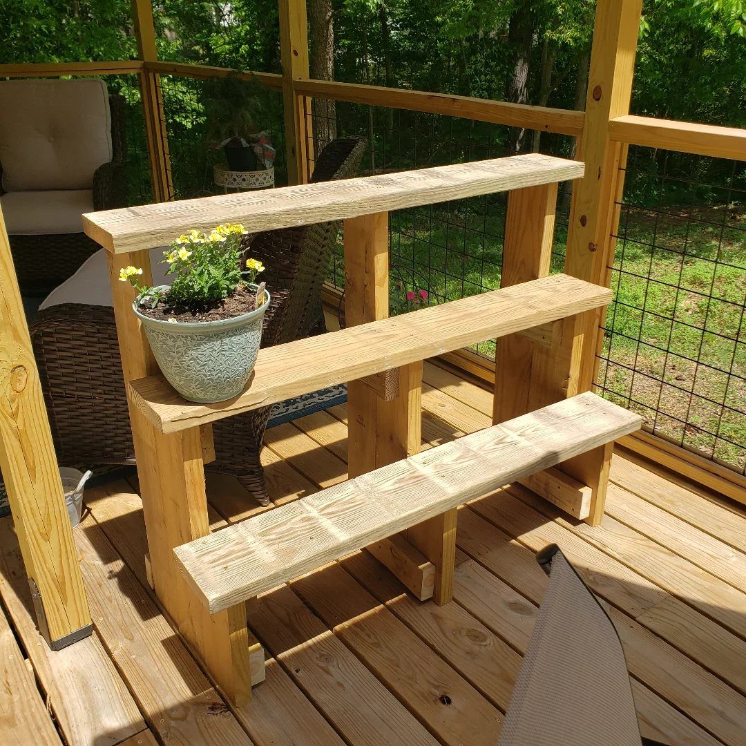 32 Mini Wood Projects for Beginners and Scrap Wood 1 Three-tiered wooden plant stand on a deck holding a pot of yellow flowers.