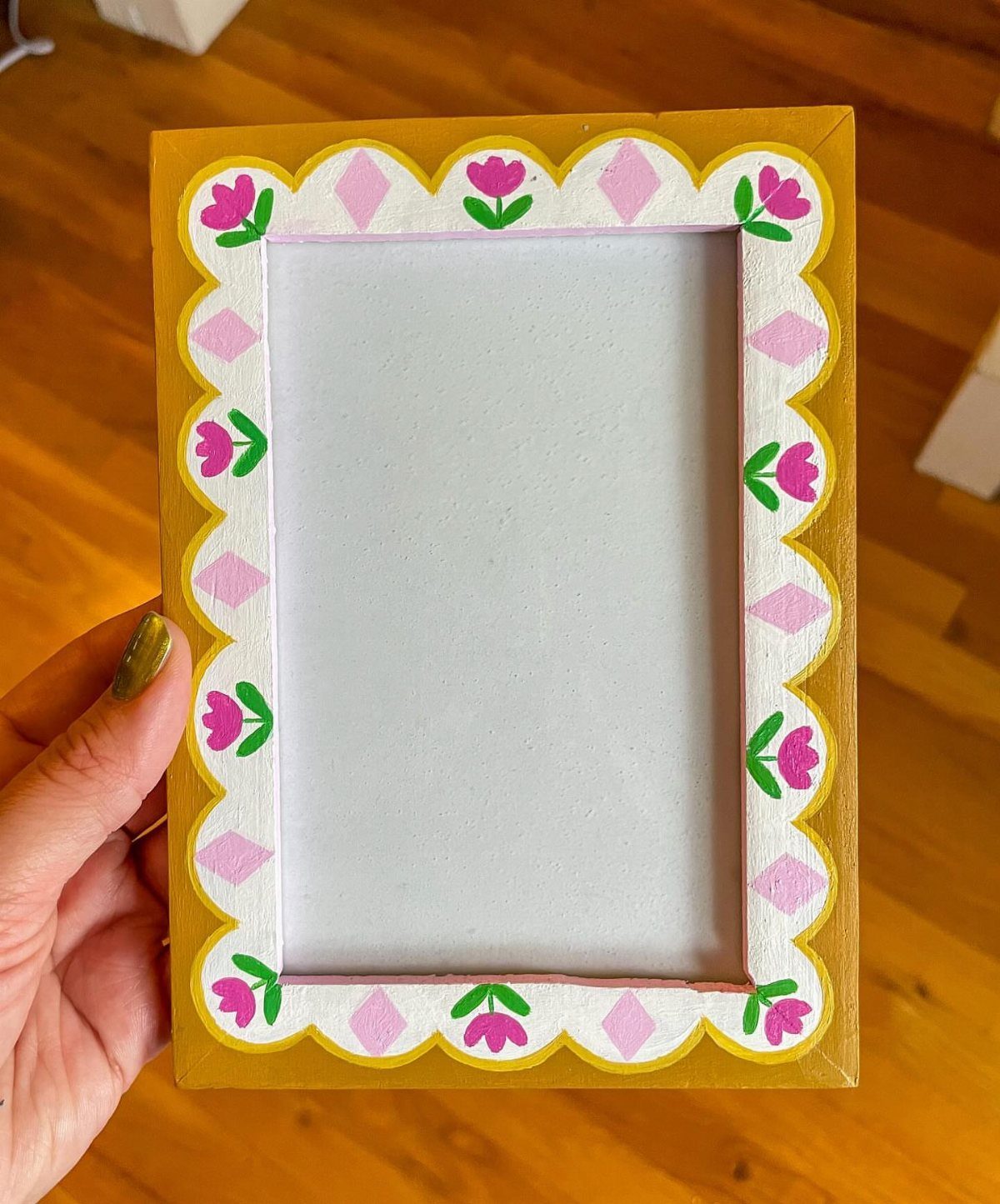 32 Mini Wood Projects for Beginners and Scrap Wood 16 Hand holding a yellow wooden picture frame with pink floral and diamond decorations.