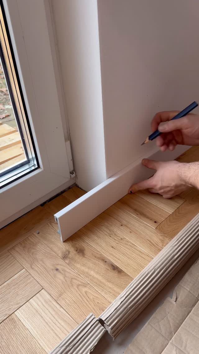 Mitered Corners for Wood: 4 Ideas for Tight Joints 2 Hands marking a white wooden baseboard with a pencil against a white wall.