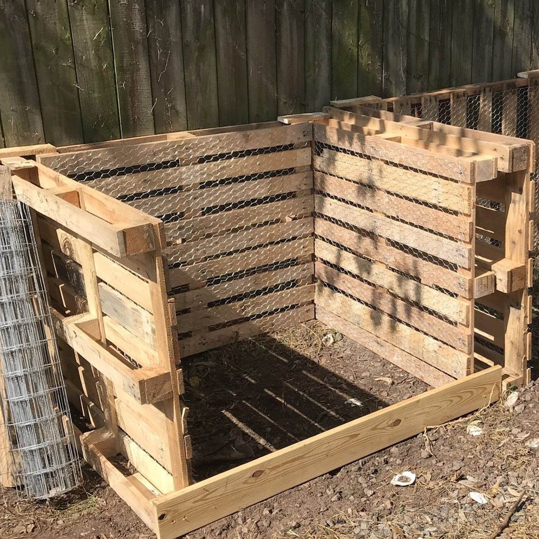 Wooden pallet compost bin with wire mesh lining in a backyard garden.