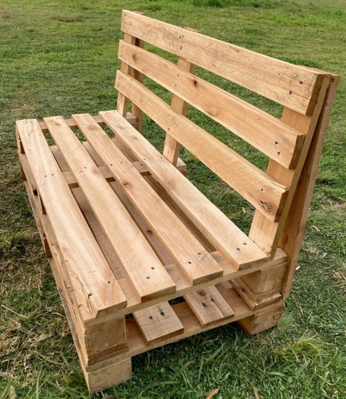 Wooden pallet chair with a slatted seat and backrest on green grass.