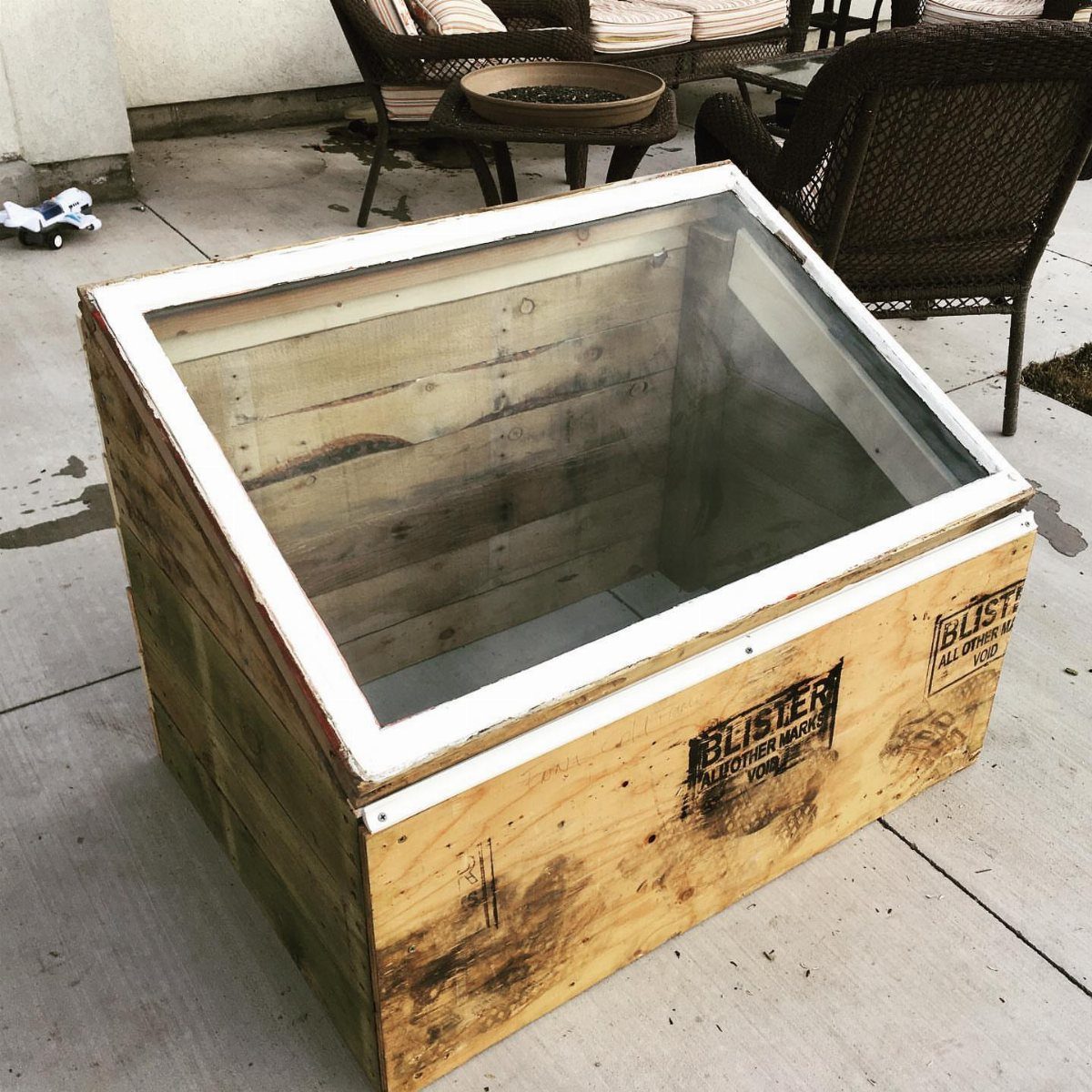 Wooden pallet cold frame with a clear top sitting on a concrete patio.