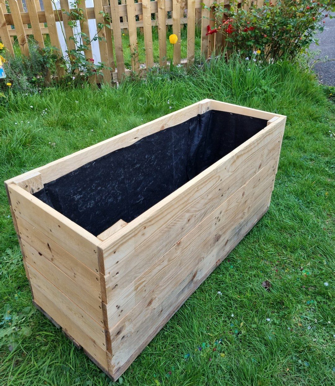 Wooden pallet planter box lined with black fabric sitting on a green lawn.