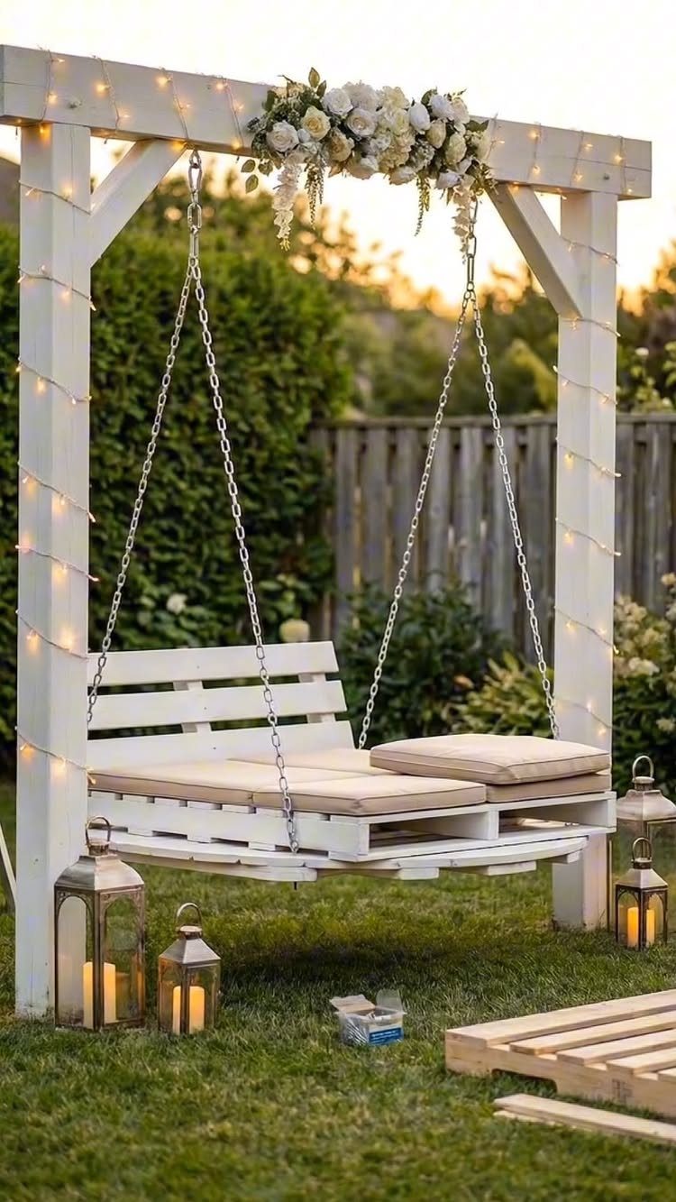 White pallet swing with cushions hanging from a floral decorated wooden frame.