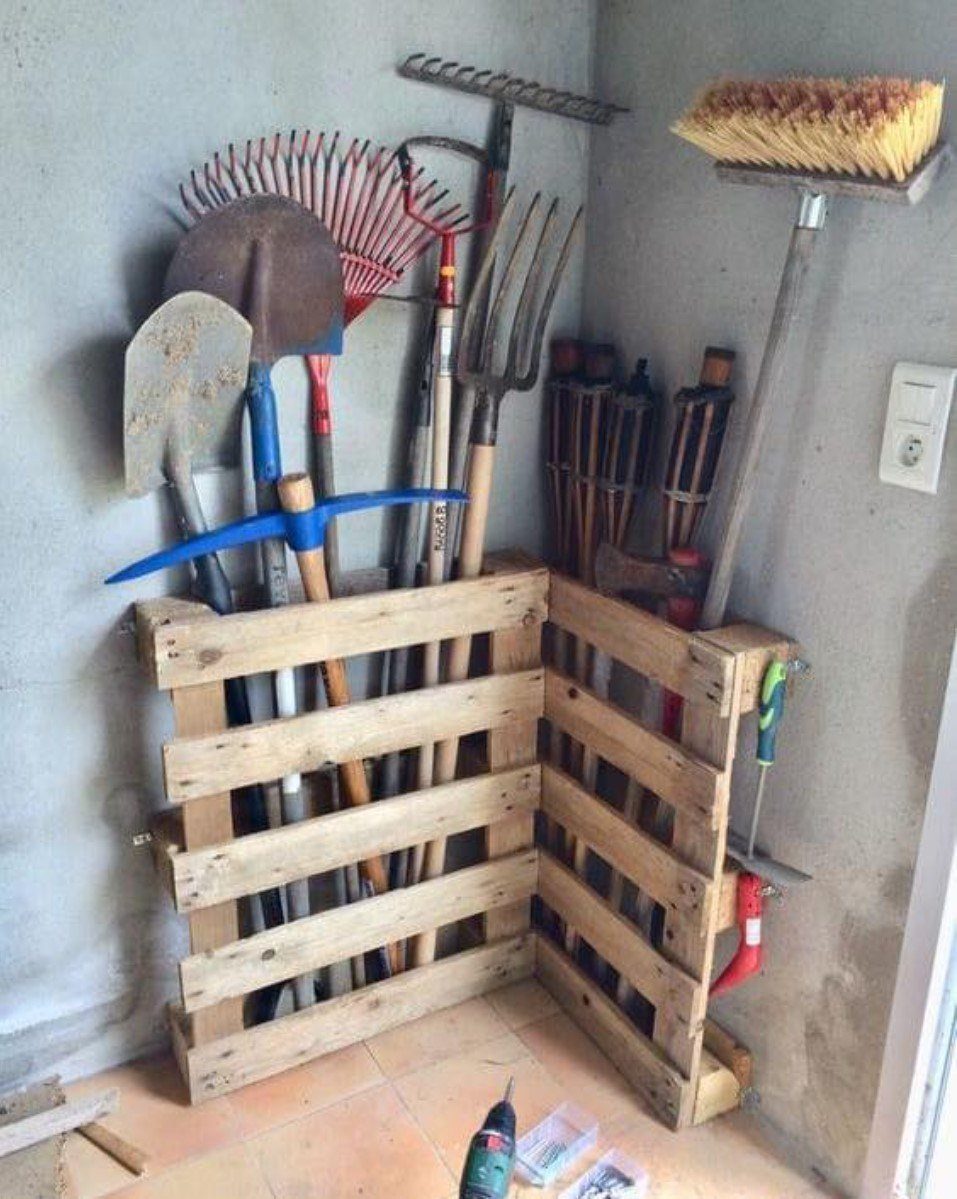 Wooden pallet tool organizers holding shovels, rakes, and a broom against a wall.