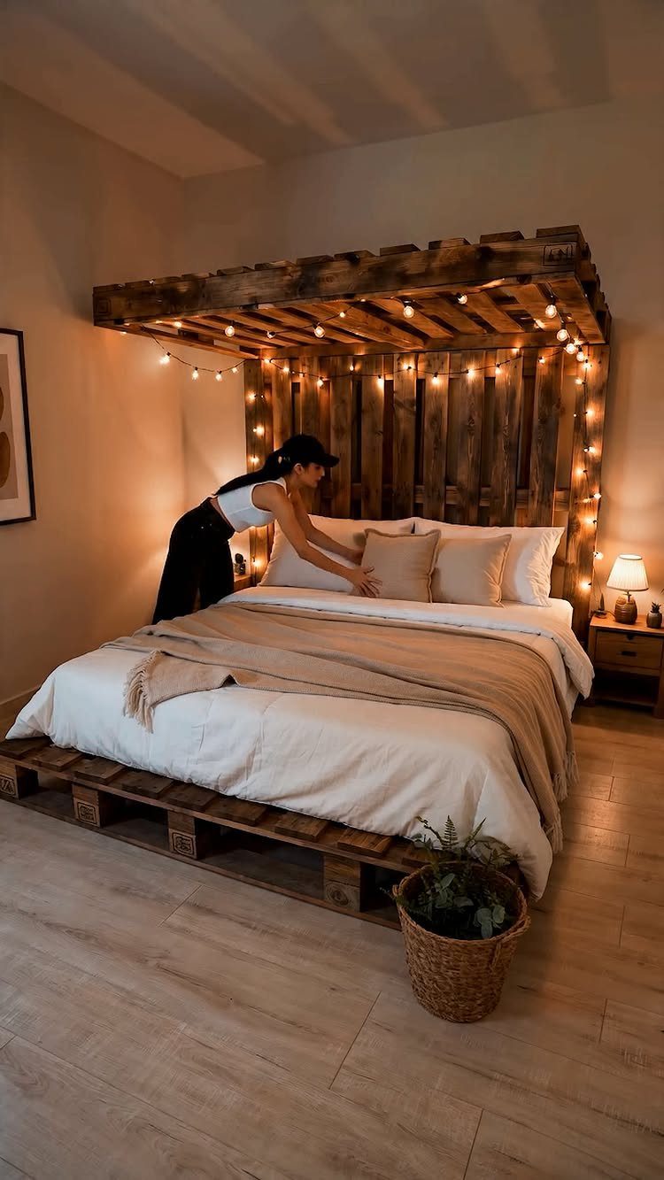 21 Pallet Wood DIY Projects for Home, Holidays and Yard 9 Woman adjusting pillows on a bed with a pallet wood frame and canopy.