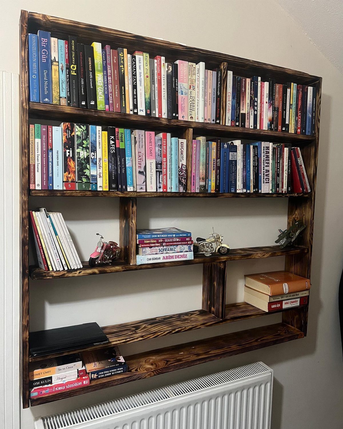 21 Pallet Wood DIY Projects for Home, Holidays and Yard 2 Dark stained pallet wood bookshelf mounted on a wall filled with colorful books.