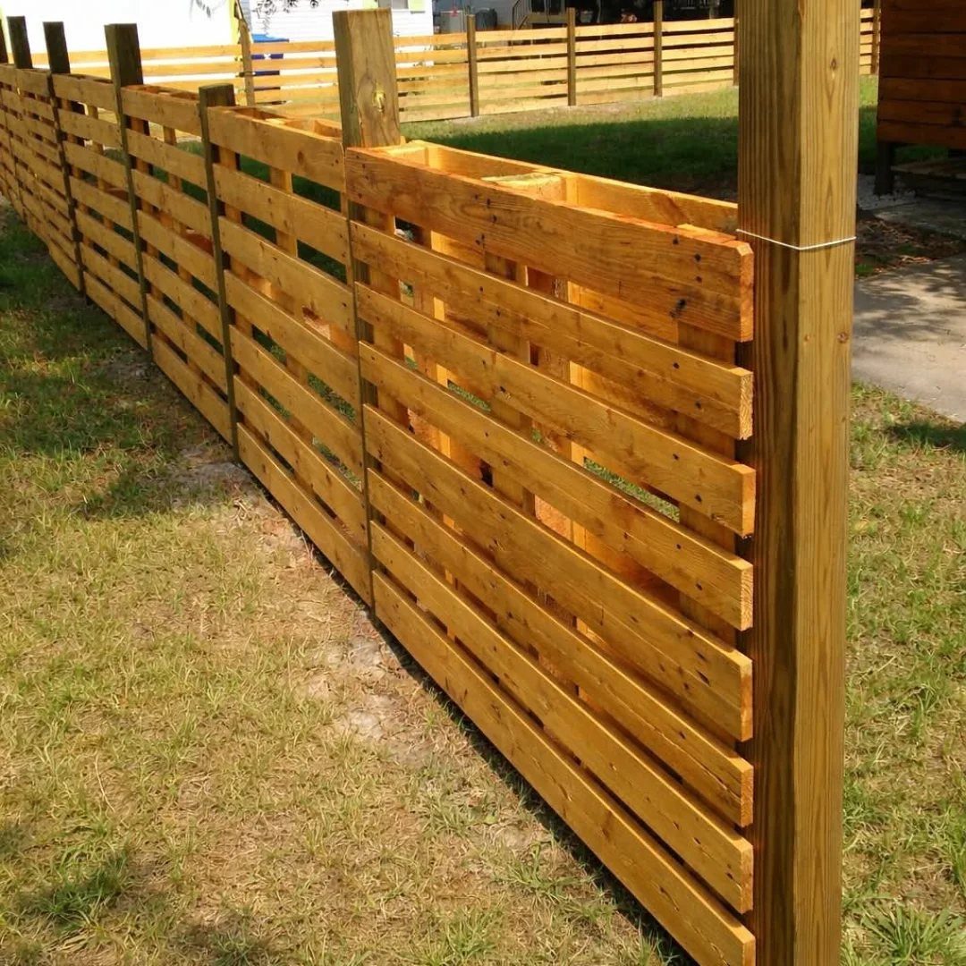 21 Pallet Wood DIY Projects for Home, Holidays and Yard 14 Wooden pallet fence with horizontal slats and thick posts on a grassy lawn.