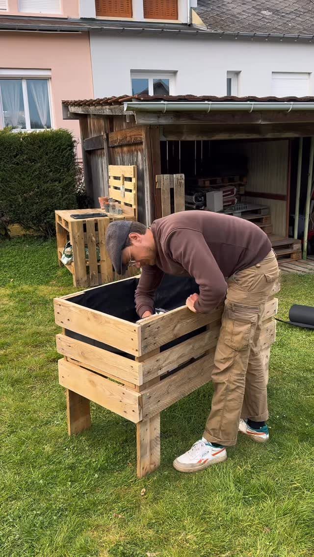 21 Pallet Wood DIY Projects for Home, Holidays and Yard 5 Man assembling a large square planter made from light-colored pallet wood on grass.