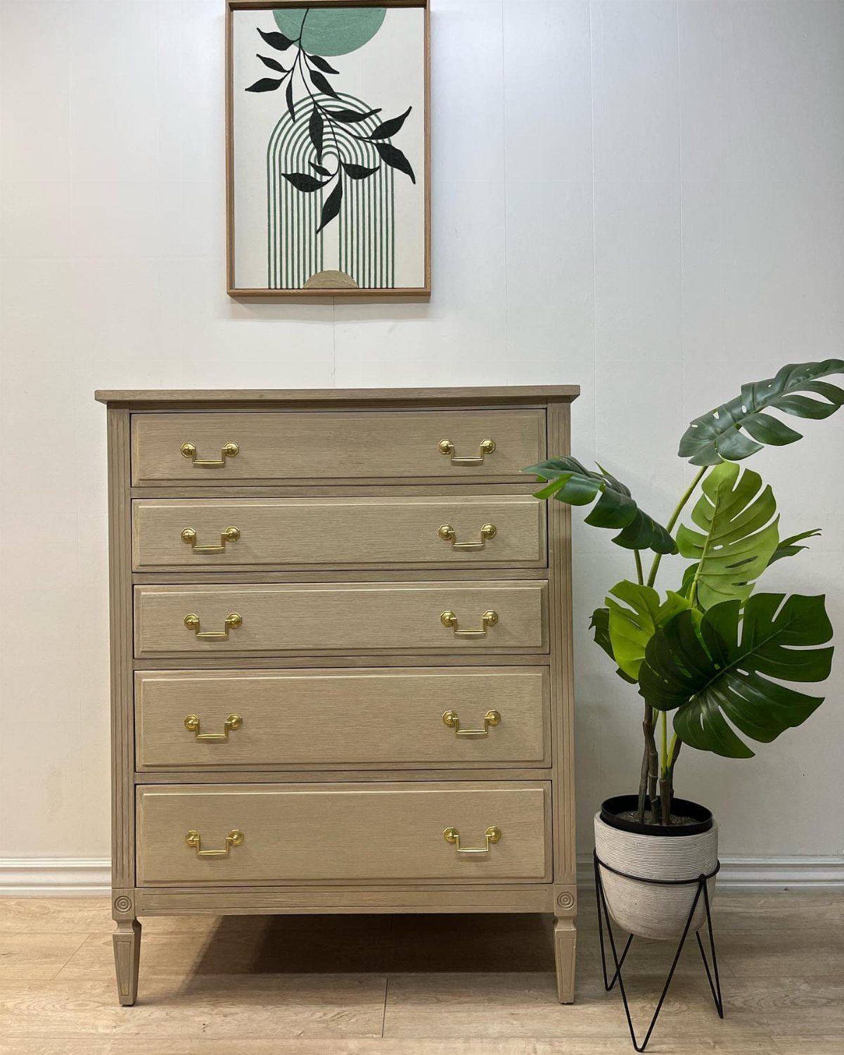 Light beige wooden dresser with gold hardware and a potted Monstera plant.