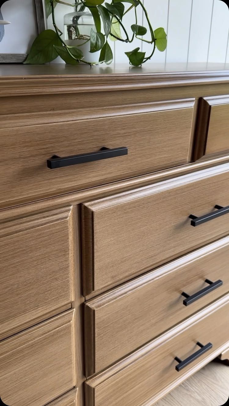 Light brown wooden dresser with a rich stained finish and black modern handles.
