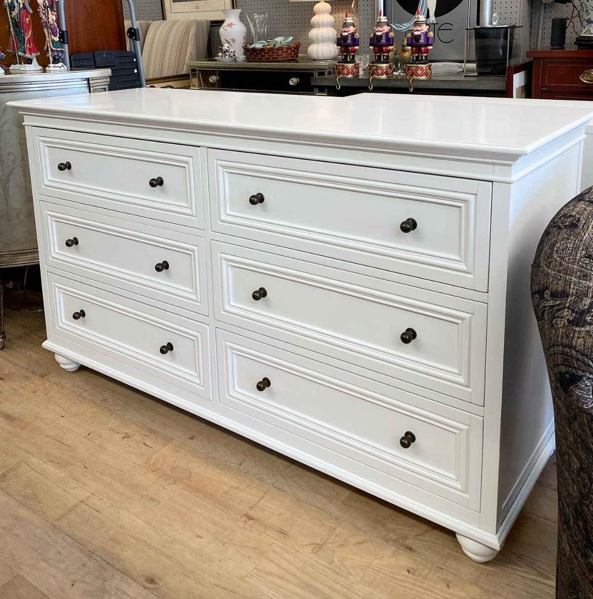 White painted dresser with decorative trim pieces on the drawer fronts and dark knobs.
