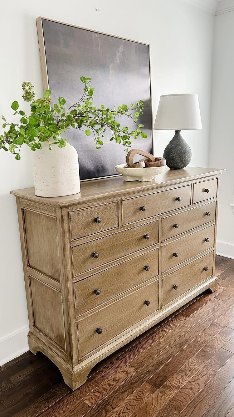 Weathered light brown wooden dresser with black knobs and home decor on top.