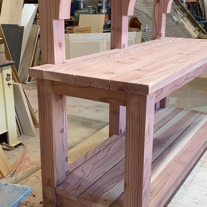 Wooden potting bench with a lower shelf inside a woodworking shop.