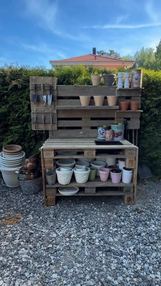 Pallet potting bench with wooden shelves holding various gardening pots on gravel ground.