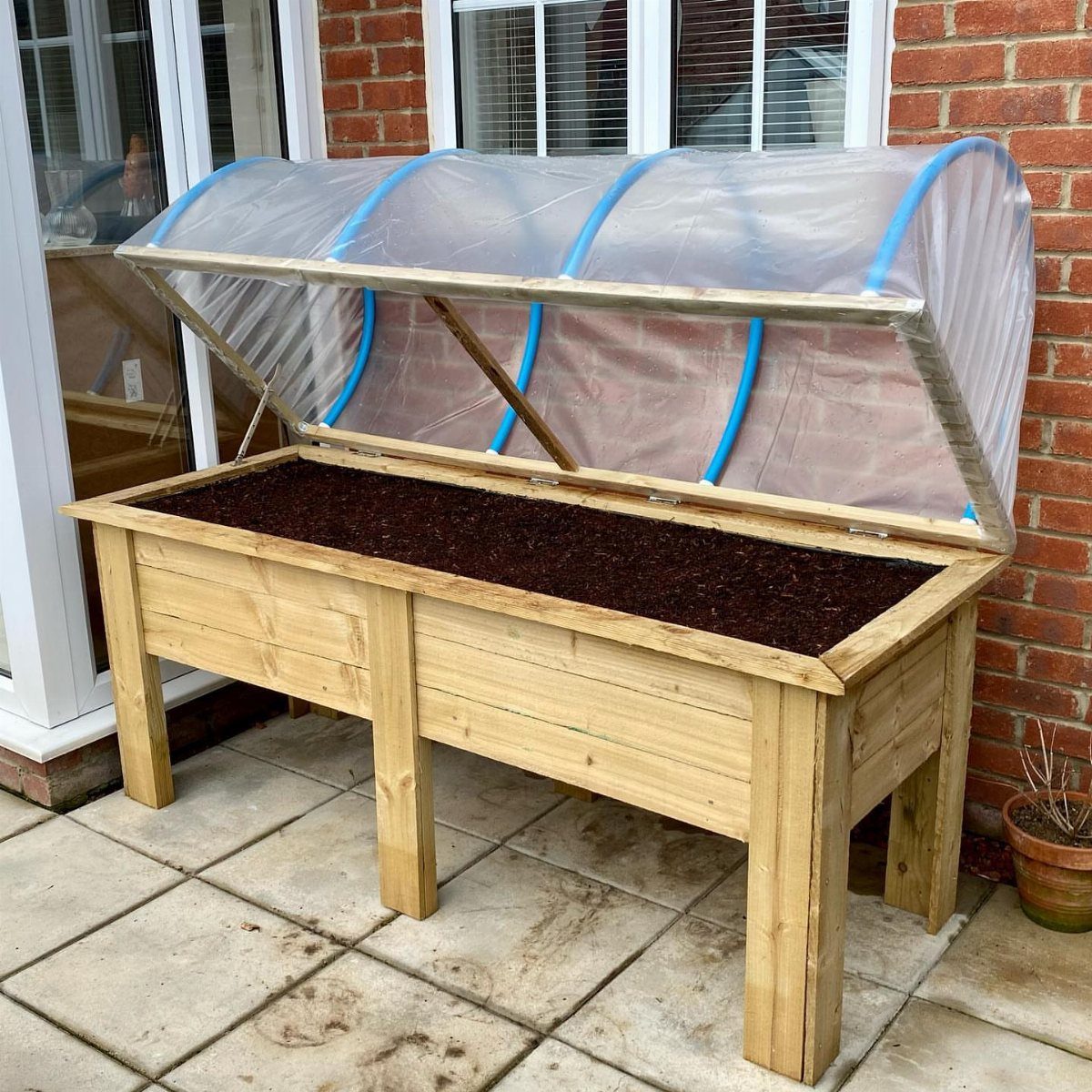 Wooden potting bench with a clear plastic cover and soil bed on a patio.