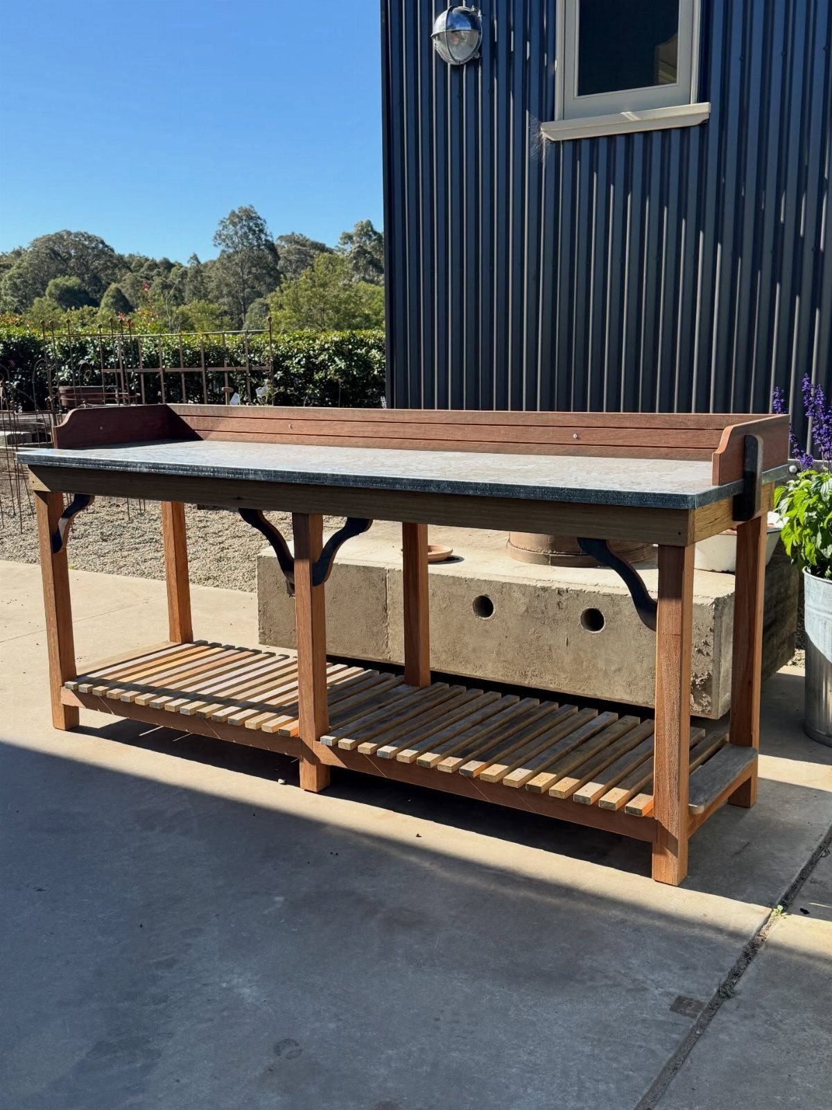 Wooden potting bench with a stone countertop and slatted lower shelf outdoors.
